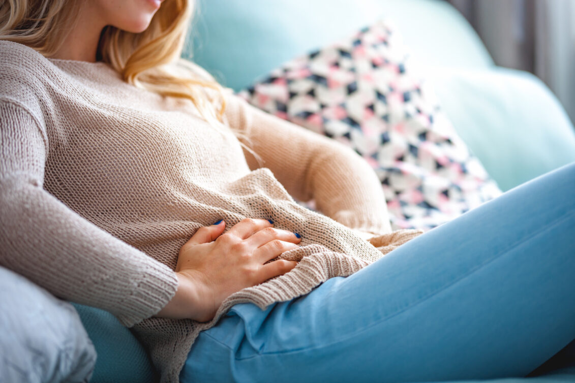 Young woman suffering from abdominal pain while sitting on sofa